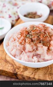 Fresh raw chopped chicken meat with seasoning in a bowl, selective focus