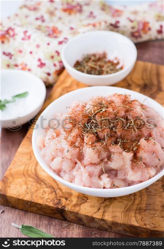 Fresh raw chopped chicken meat with seasoning in a bowl, selective focus
