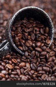 Fresh raw coffee beans in black ceramic cup inside coffee beans background. Macro