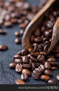 Fresh raw coffee beans in woode scoop on black background. Macro