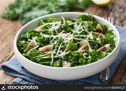 Fresh raw curly kale and sauteed mushroom salad with grated parmesan served in bowl, photographed on wood with fresh kale leaves and lemon in the back  Selective Focus, Focus in the middle of the image . Fresh Curly Kale and Mushroom Salad with Parmesan