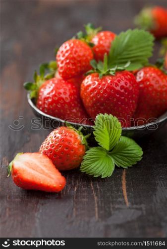 Fresh raw farm organic strawberries with leaf in steel bowl on wooden background. Macro