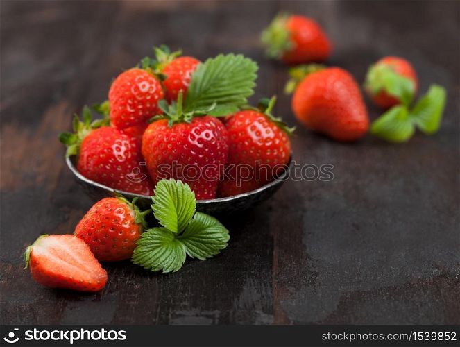 Fresh raw farm organic strawberries with leaf in steel bowl on wooden background. Top view