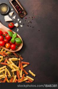 Fresh raw fusilli pasta with tomatoes in wooden bowl with oil and parmesan cheese with salt on dark brown background. Top view