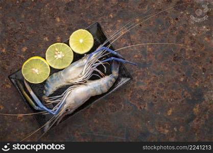 fresh raw giant freshwater prawns in black rectangular ceramic plate with slice lime on rusty texture background with copy space for text, top view, river prawn