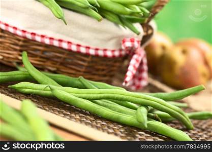 Fresh raw green beans in front of a basket with potatoes in the back (Selective Focus, Focus on the long bean one third into the image ). Green Beans