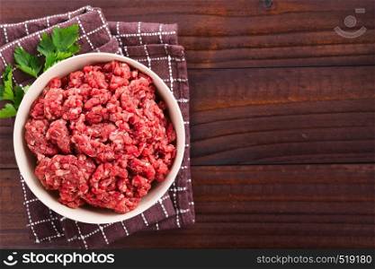 Fresh raw ground or minced beef meat in bowl, photographed overhead on dark wood with copy space on the side (Selective Focus, Focus on the meat). Fresh Raw Ground Beef Meat
