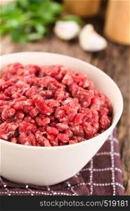 Fresh raw ground or minced beef meat in bowl, seasonings (salt, pepper), garlic and fresh parsley in the back (Selective Focus, Focus one third into the meat). Fresh Raw Ground Beef Meat