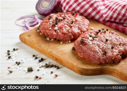 Fresh raw home-made minced beef steak burger cutlet with spices and onion on a cutting board, on a white wooden table. raw home-made beef burger cutlet