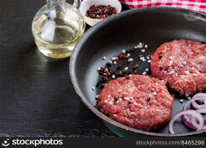 Fresh raw home-made minced beef steak burger cutlet with spices In a frying pan, on a black slate table, copy space, top view. raw home-made beef burger cutlet