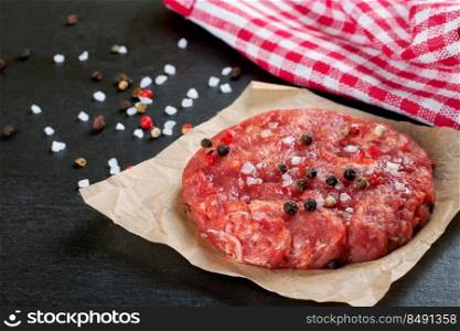 Fresh raw home-made minced beef steak burger with spices, on a black slate table, copy space, top view. raw home-made beef burger cutlet