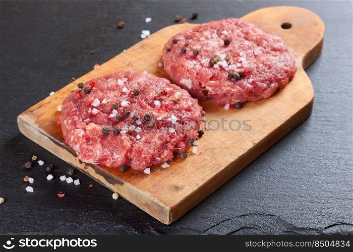 Fresh raw home-made minced beef steak burger with spices, on a cutting board on black slate table, copy space, top view. raw home-made beef burger cutlet