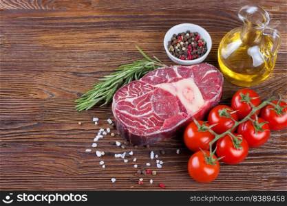 Fresh raw meat beef steak with bone with spices, rosemary, tomatoes and olive oil on brown wooden background. cooking ingredients. Top view, flat lay, mockup with copy space for text. Cooking ingredients. Fresh raw meat beef steak with bone.