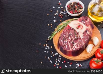 Fresh raw meat beef steak with bone with spices, rosemary, tomatoes, garlic and olive oil on wooden cutting board and on the black slate surface. cooking ingredients. Top view. Flat lay.. Cooking ingredients. Fresh raw meat beef steak with bone.