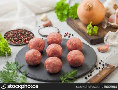 Fresh raw meatballs on stone board with pepper, salt and garlic on light table background with dill,parsley and dill. Top view