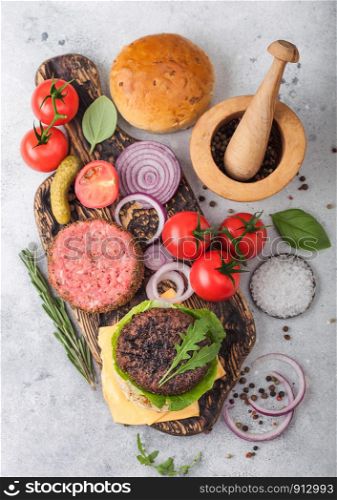 Fresh raw minced and grilled pepper beef burgers on vintage chopping board with buns onion and tomatoes on wooden background.Mortar with pestle with pickles and basil. Top view