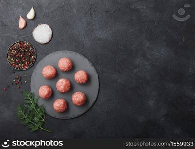 Fresh raw minced beef meatballs on round board with pepper, salt and garlic on black background. Space for text