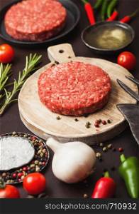 Fresh raw minced homemade farmers grill beef burger on round chopping board with spices and herbs and fork and knife on brown board.