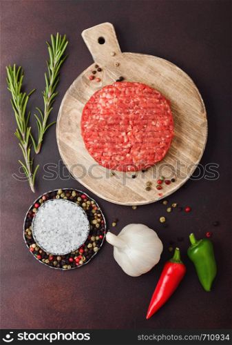 Fresh raw minced homemade farmers grill beef burger on round chopping board with spices and herbs and garlic on brown background.