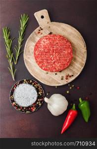 Fresh raw minced homemade farmers grill beef burger on round chopping board with spices and herbs and garlic on brown background.