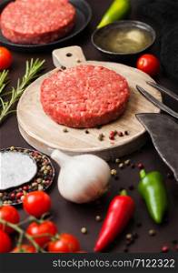 Fresh raw minced homemade farmers grill beef burger on round chopping board with spices and herbs and fork and knife on brown board.