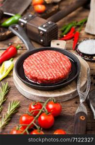 Fresh raw minced homemade farmers grill beef burgers on round chopping board and frying pan with spices and herbs and meat hatchet on wooden board.