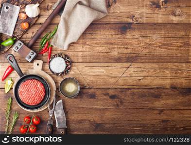 Fresh raw minced homemade farmers grill beef burgers on round chopping board and frying pan with spices and herbs and meat hatchet on wooden board. Space for text