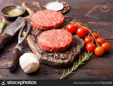 Fresh raw minced homemade farmers grill beef burgers on vintage chopping board with spices and herbs and fork with knife on wooden board.