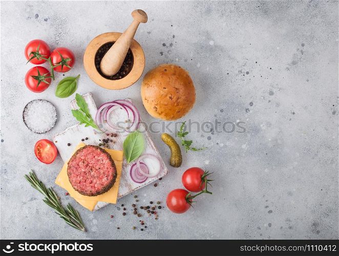 Fresh raw minced pepper beef burger on vintage chopping board with buns onion and tomatoes on wooden background.Mortar with pestle with pickles and basil. Space for text