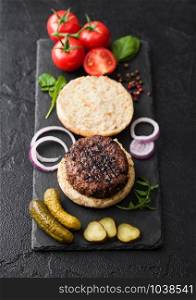 Fresh raw minced pepper beef burgers on vintage chopping board with buns onion and tomatoes on wood background. Top view