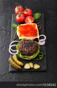 Fresh raw minced pepper beef burgers on vintage chopping board with buns onion and tomatoes on wood background. Top view