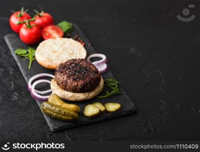 Fresh raw minced pepper beef burgers on vintage chopping board with buns onion and tomatoes on wood background. Space for text