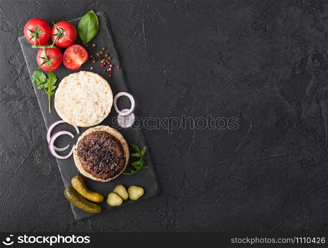 Fresh raw minced pepper beef burgers on vintage chopping board with buns onion and tomatoes on wood background. Space for text