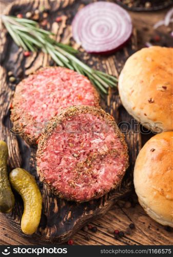 Fresh raw minced pepper beef burgers on vintage chopping board with buns onion and tomatoes on wood background.