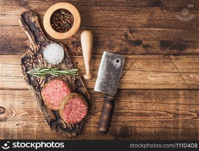 Fresh raw minced pepper beef burgers on vintage chopping board with mortar and pestle and meat hatchet on wood background.