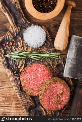 Fresh raw minced pepper beef burgers on vintage chopping board with mortar and pestle and meat hatchet on wood background.