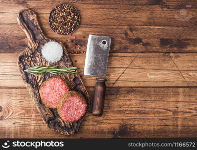 Fresh raw minced pepper beef burgers on vintage chopping board with spices and herbs and meat hatchet on wood background.