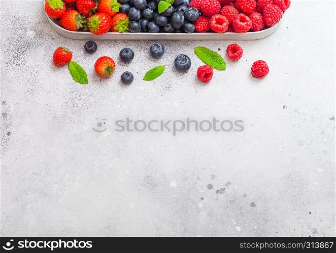 Fresh raw organic berries in in stainless steel tray on stone kitchen table background. Space for text. Top view. Strawberry, Raspberry, Blueberry and Mint leaf
