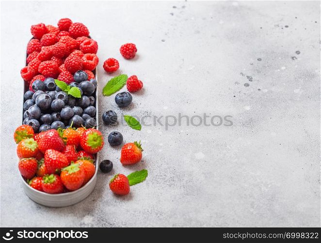 Fresh raw organic berries in in stainless steel tray on stone kitchen table background. Space for text. Top view. Strawberry, Raspberry, Blueberry and Mint leaf