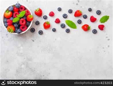 Fresh raw organic berries in white ceramic bowl on kitchen table background. Space for text. Strawberry, Raspberry, Blueberry and Mint leaf