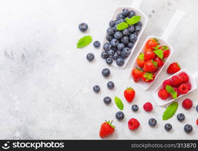 Fresh raw organic berries in white scoop spoon on kitchen table. Space for text. Top view. Strawberry, Raspberry, Blueberry and Mint leaf