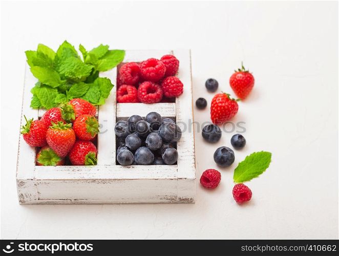Fresh raw organic berries in white wooden box on kitchen table background. Strawberry, Raspberry, Blueberry and Mint leaf