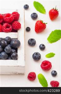 Fresh raw organic berries in white wooden box on kitchen table background. Strawberry, Raspberry, Blueberry and Mint leaf