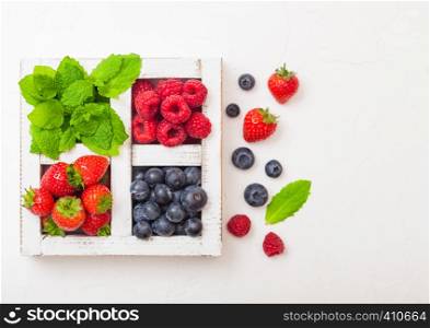 Fresh raw organic berries in white wooden box on kitchen table background. Space for text. Strawberry, Raspberry, Blueberry and Mint leaf