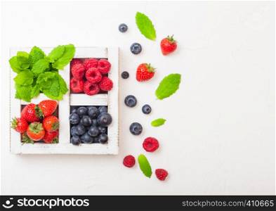 Fresh raw organic berries in white wooden box on kitchen table background. Space for text. Strawberry, Raspberry, Blueberry and Mint leaf