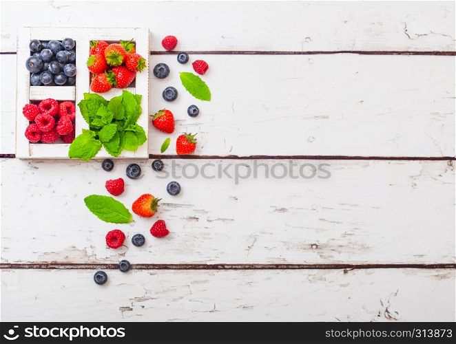 Fresh raw organic berries in white wooden box on wood background. Space for text. Strawberry, Raspberry, Blueberry and Mint leaf