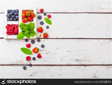 Fresh raw organic berries in white wooden box on wood background. Space for text. Strawberry, Raspberry, Blueberry and Mint leaf