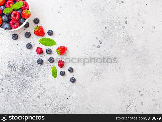 Fresh raw organic berries isolated in white ceramic bowl on kitchen table background. Strawberry, Raspberry, Blueberry and Mint leaf