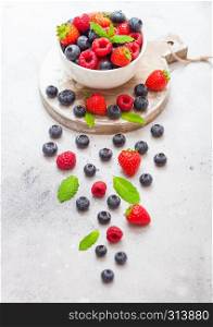 Fresh raw organic berries isolated in white ceramic bowl on round wooden board. Strawberry, Raspberry, Blueberry and Mint leaf
