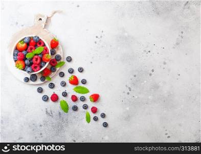 Fresh raw organic berries isolated in white ceramic bowl on round wooden board. Space for text. Strawberry, Raspberry, Blueberry and Mint leaf